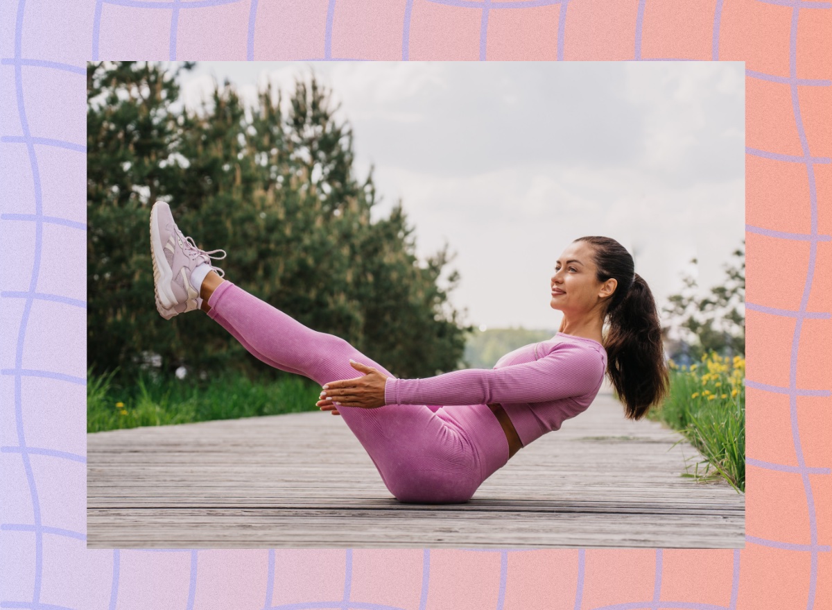 fit woman in pink yoga apparel doing boat pose on boardwalk out to a lake or beach