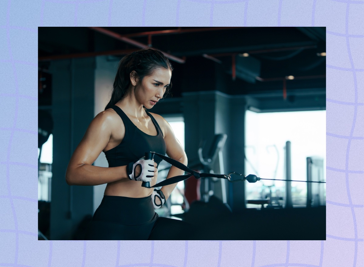 focused brunette woman doing a single-arm cable row exercise in dark gym