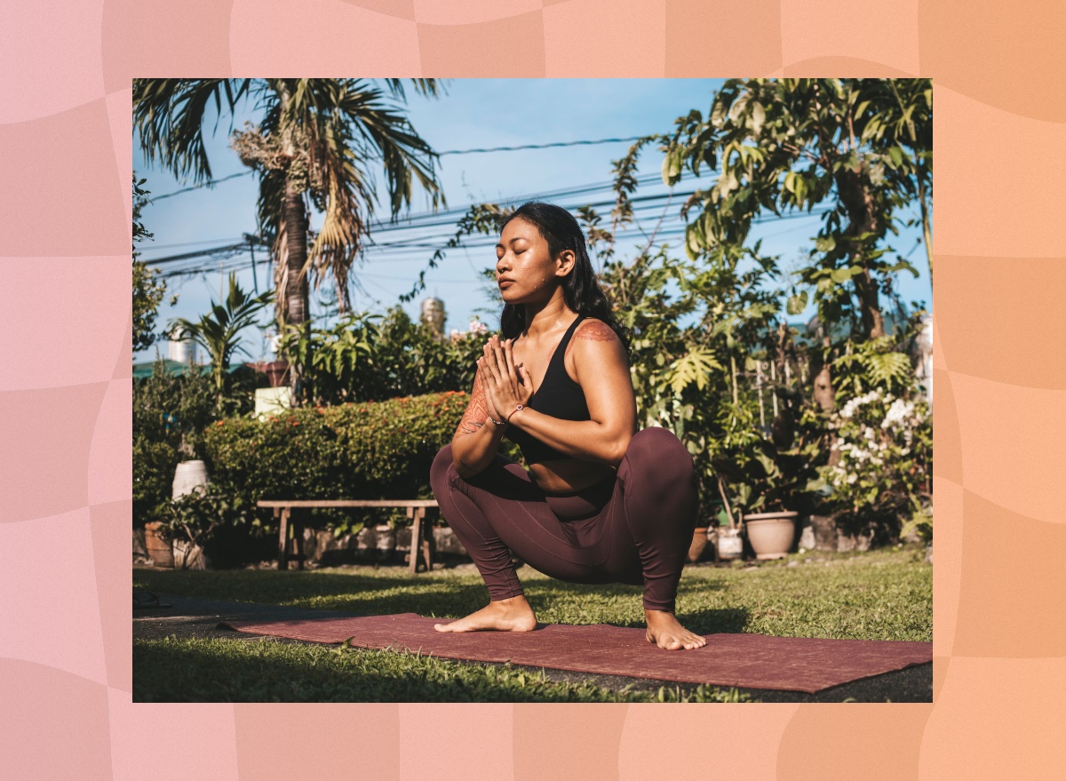 peaceful brunette woman doing yogi squat on mat outdoors in yard on sunny day