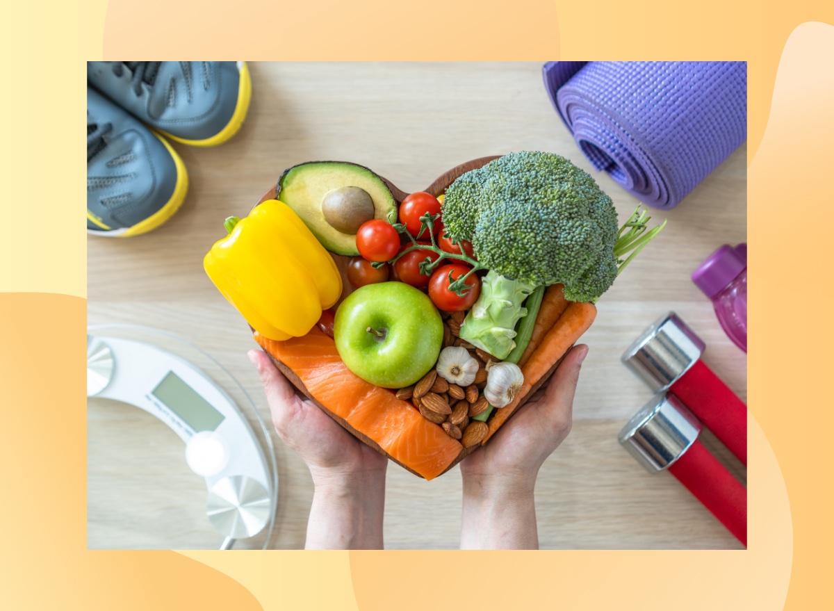 close-up of woman's hands holding a bowl of healthy foods over a floor with a scale, sneakers, and weights