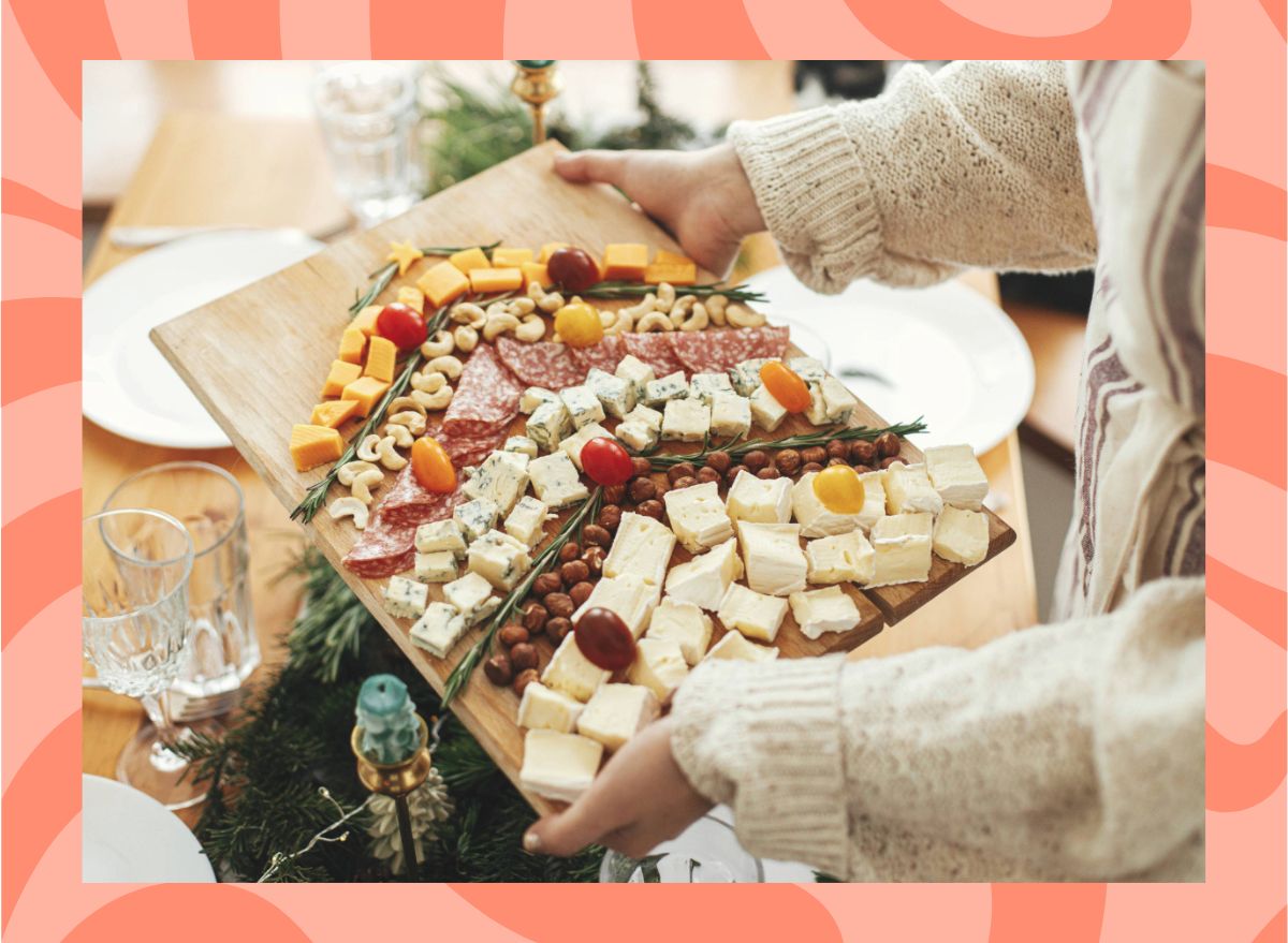 woman holding a cheese board set against a red designed background