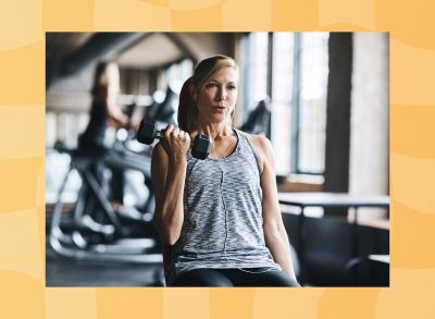 focused, middle-aged woman lifting weights seated at a workout bench in a gym's weight room