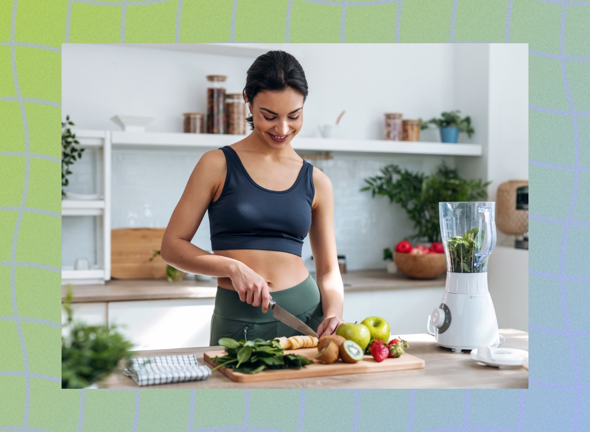 fit, happy brunette woman in sports bra and leggings cutting up fruits and veggies for a smoothie in her bright kitchen