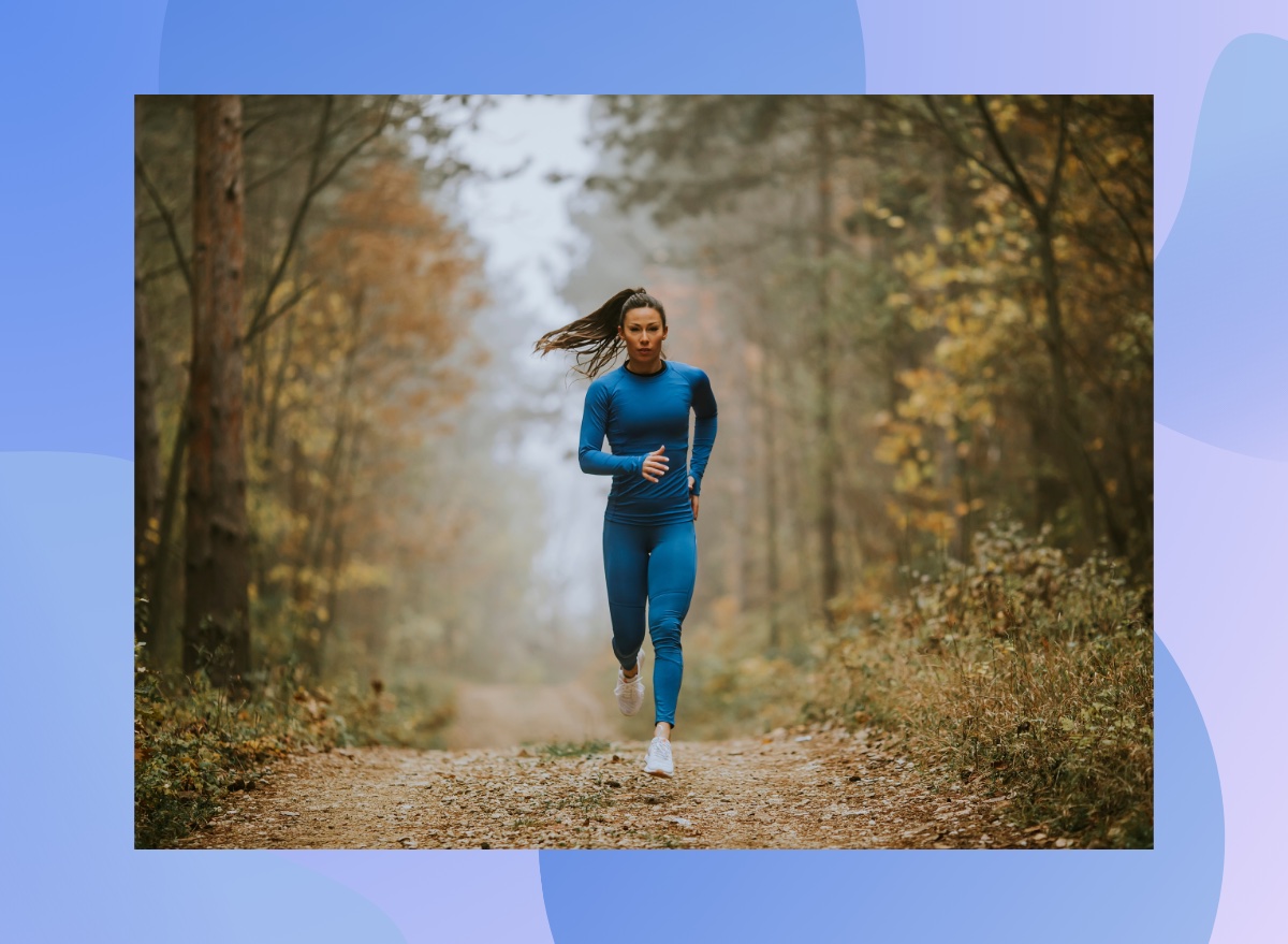 fit brunette woman in blue athletic top and leggings doing a trail run on a cloudy autumn day