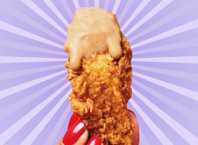 A chicken tender from KFC, dripping with sauce and held in a woman's fingers, all set against a vibrant purple background.