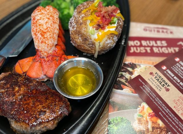 Outback steak and lobster with baked potato and broccoli on table next to menus