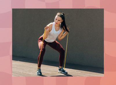 fit, focused brunette woman doing resistance band squat exercise outdoors