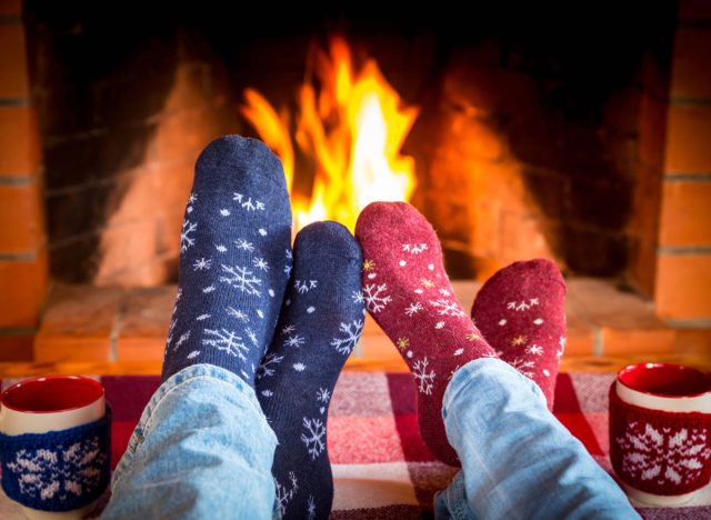 close-up of couples' feet in Christmas socks in front of the fire next to Christmas mugs