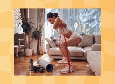 fit, determined brunette woman doing resistance band squats in bright living room