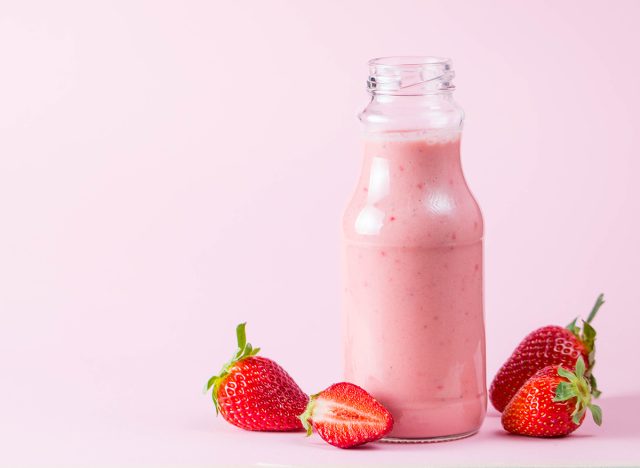 Glass of fresh strawberry milkshake, smoothie and fresh strawberries on pink, white and wooden background. Healthy food and drink concept.