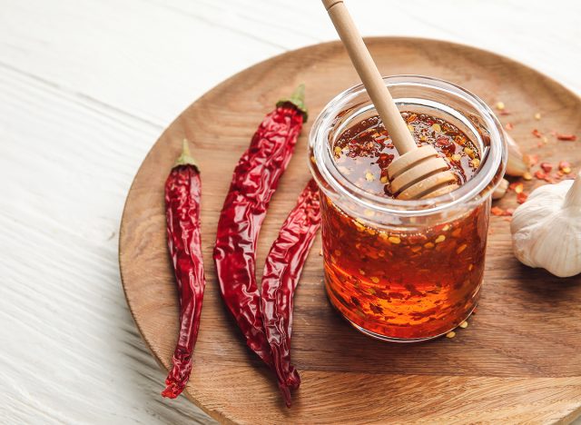 Plate with hot honey, garlic and dry chili peppers on light wooden background