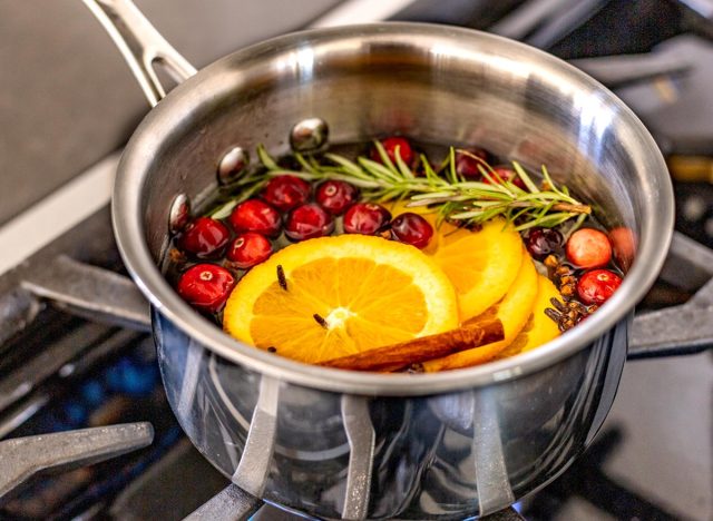 Sliced oranges, cranberries, rosemary and cinnamon sticks simmering on a gas stove with a blue flame in a metal saucepan