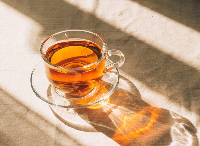 A cup of tea in glass cup and saucer illuminated by warm sunlight on a light table. Horizontal frame, copy space