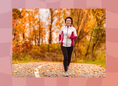 happy, fit middle-aged woman running outdoors on road on autumn day, surrounded by foliage