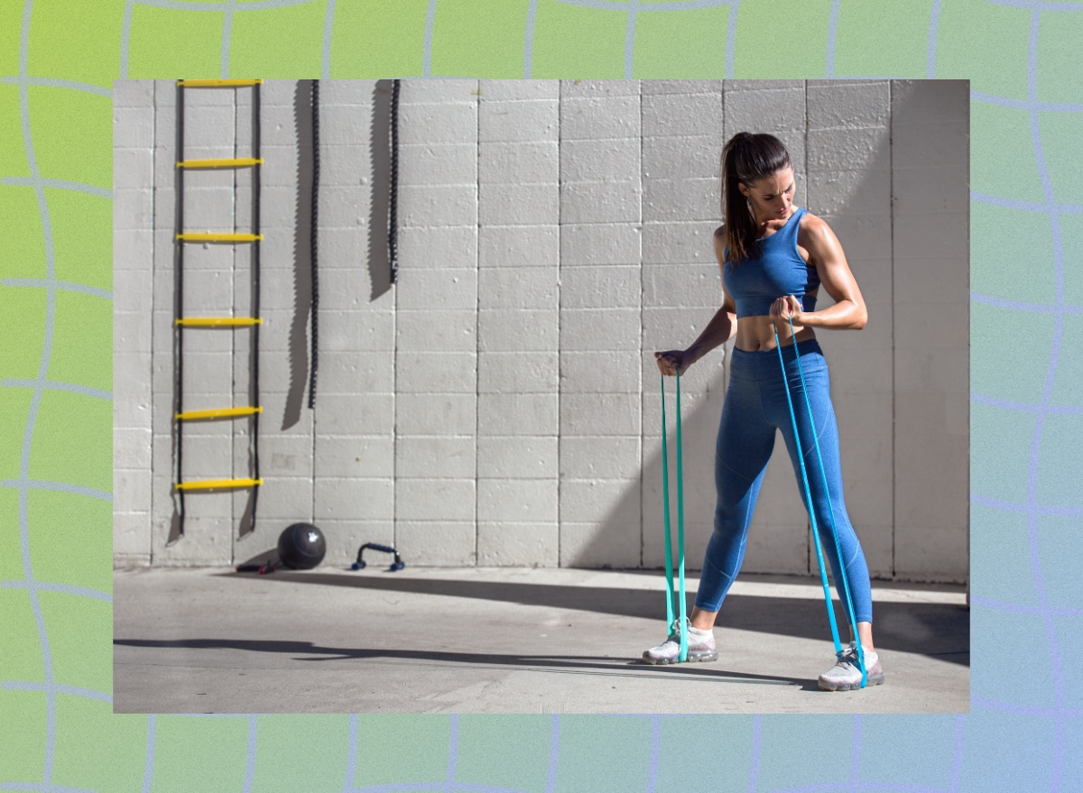 fit woman training with resistance bands, doing arm exercises outdoors