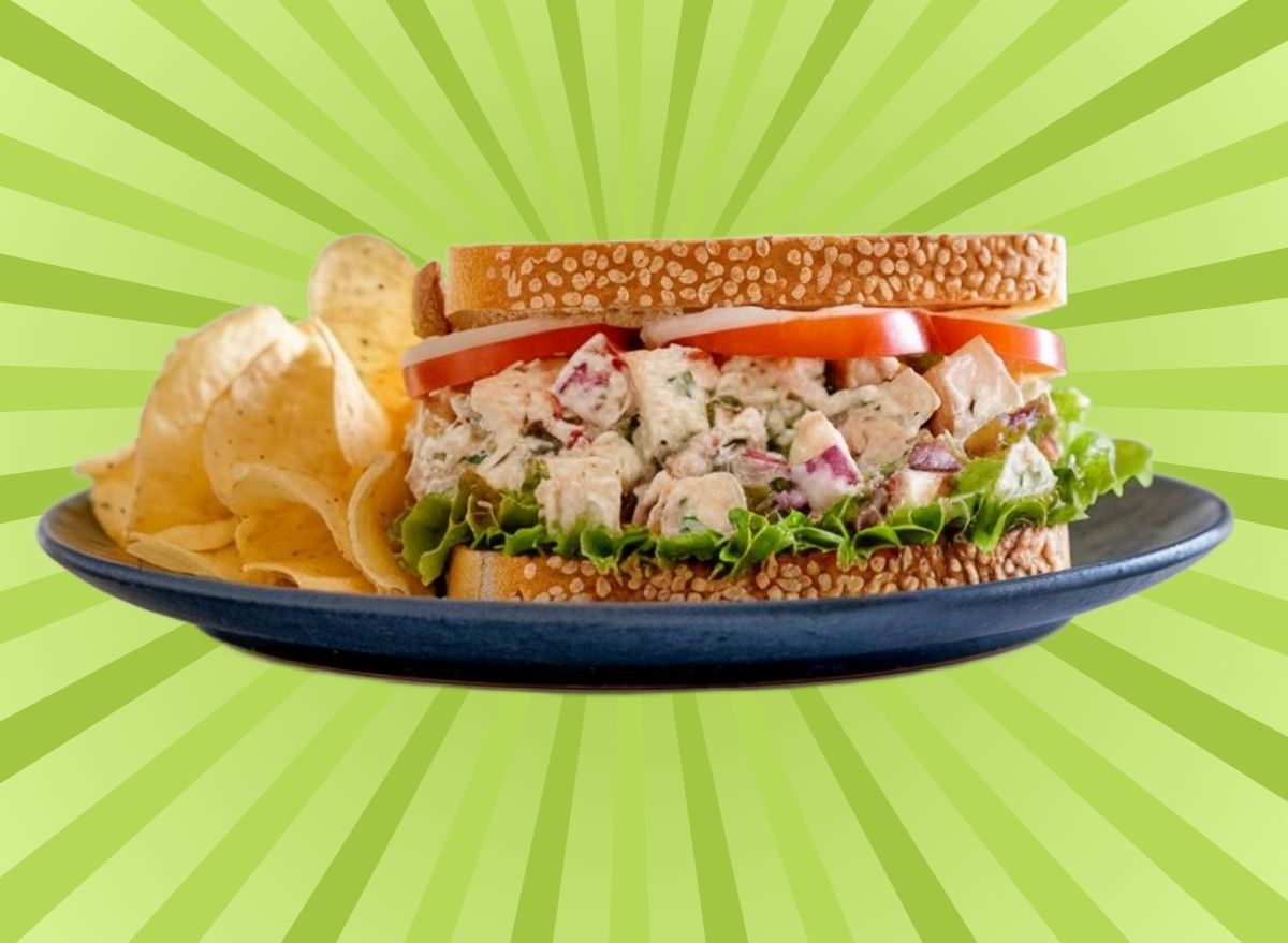 A chicken salad sandwich with chips on a plate set against a vibrant background.