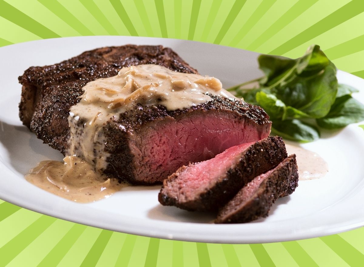 A dry-aged steak with cream sauce on a white plate, set against a vibrant background.