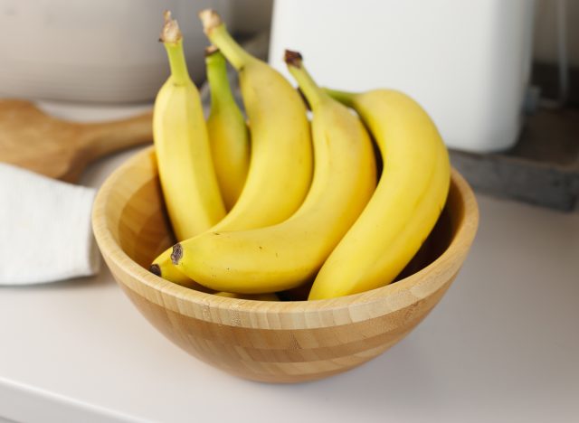 Bunch of bananas in a wooden bowl on a kitchen counter.