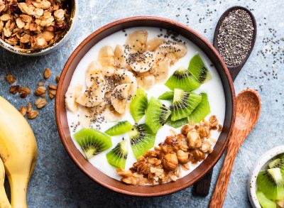 bowl of yogurt with banans chia seeds kiwis nuts and granols