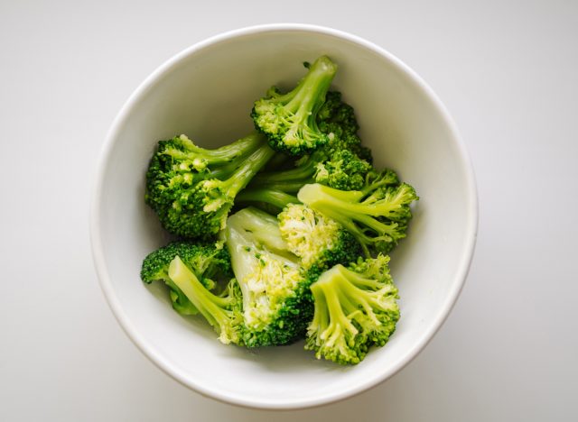 A bowl of cooked green broccoli, shot from above on a light background. Boiled broccoli vegetable in white small bowl for healthy food concept in top view.