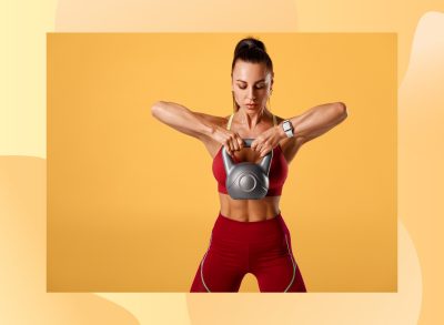 fit brunette woman lifting kettlebell in front of yellow backdrop