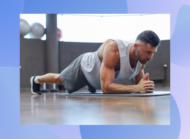 muscular, determined man holding a forearm plank on yoga mat in workout space