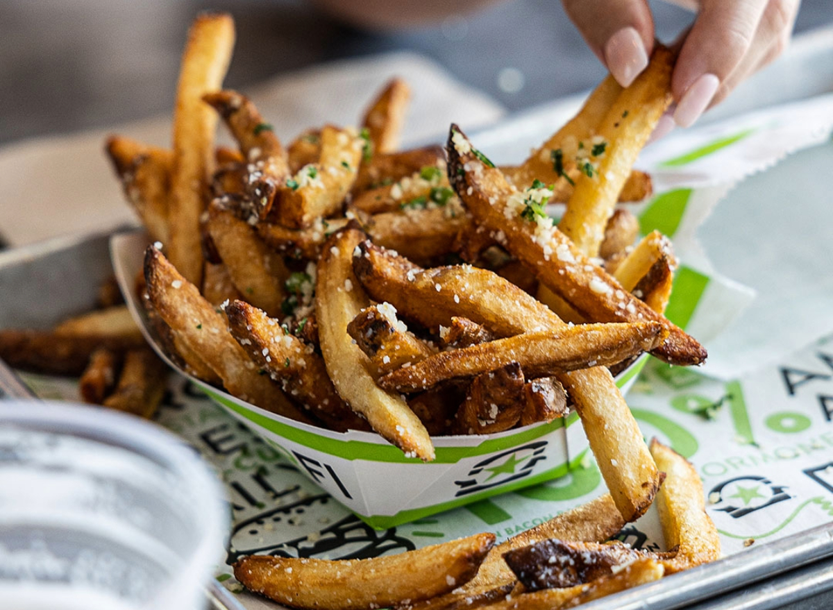 person taking a burgerfi fry from carton