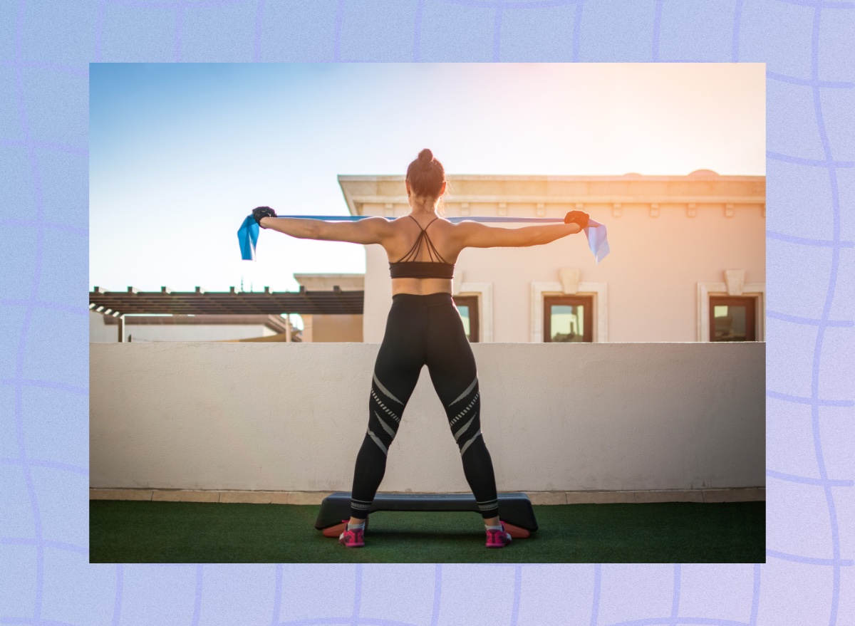 back view of fit brunette woman doing resistance band arm and back exercise on turf rooftop gym