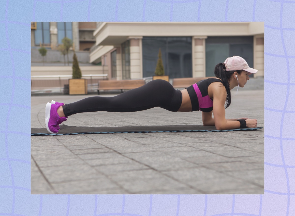 fit brunette woman doing a forearm plank on yoga mat in town square