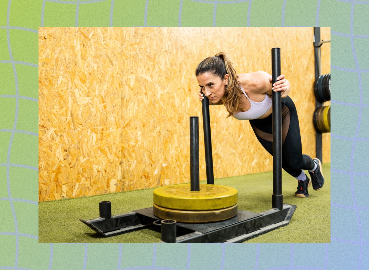 fit, focused woman doing sled push exercise on turf