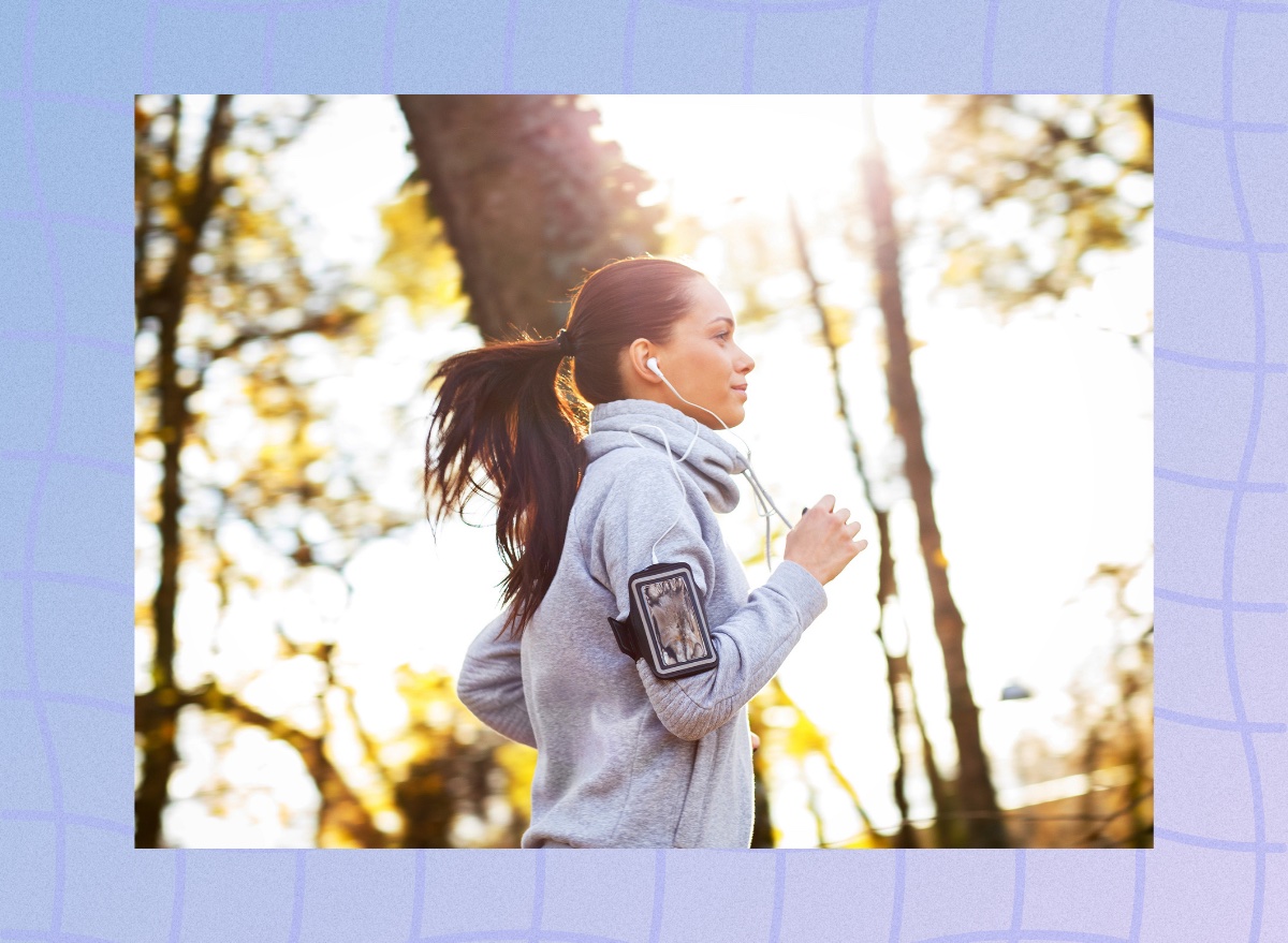 close-up of focused brunette woman in sweatshirt running outdoors through woods for exercise