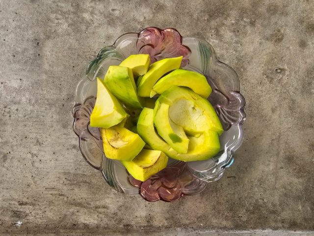 Sliced ​​avocado in glass bowl on cement table from top view