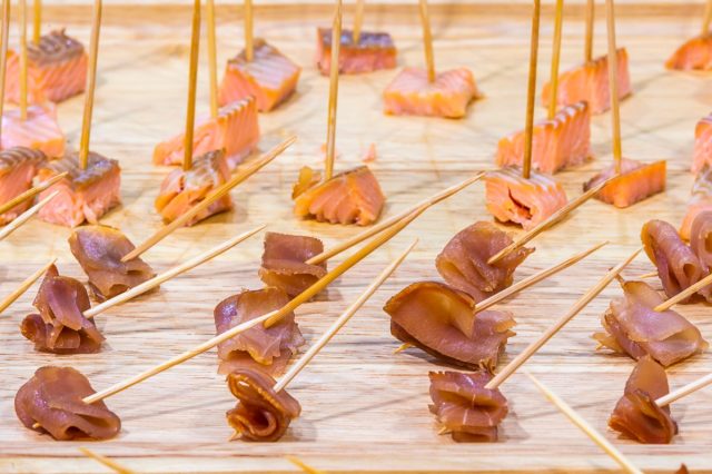 Advertising, Business, Food, Health Concept - Offering food samples to customers in shop. Smoked tuna and Smoked salmon on a wooden stick. Select focus