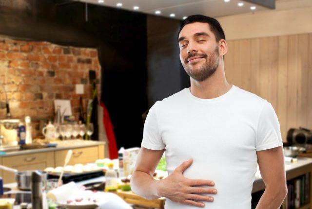 happy full man touching his tummy over kitchen background