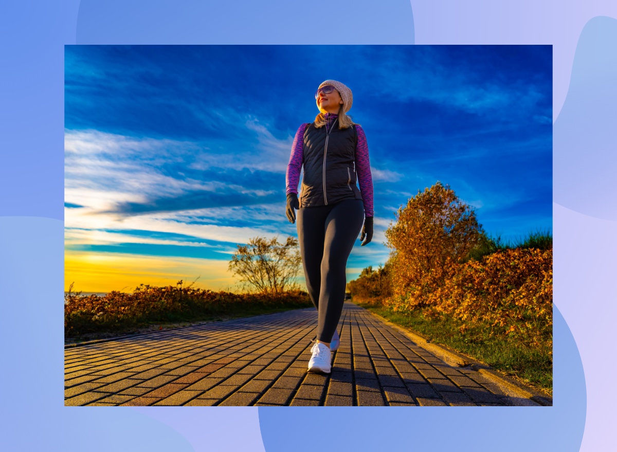 fit, middle-aged woman bundled up and walking on path by the water on fall afternoon at sunset