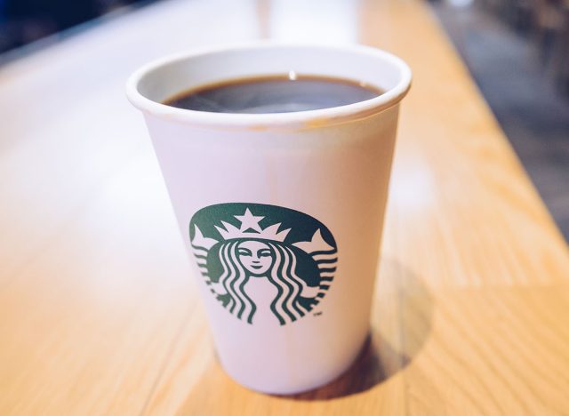 Starbucks paper cup contain hot black coffee serving on the wooden table in Starbucks coffee shop.