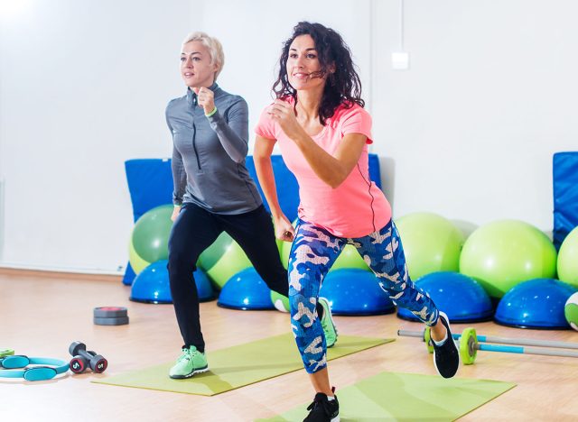 Two athletic female friends working out in a gym doing reverse lunge knee-up exercise