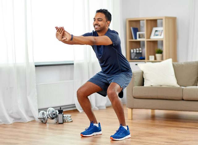 sport and healthy lifestyle concept - smiling indian man with fitness tracker exercising and doing squats at home