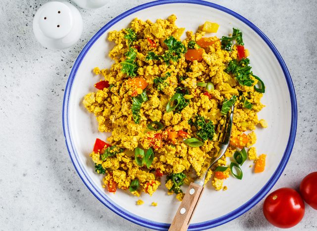 Tofu scramble with vegetables in white plate. Vegan Alternative food concept.