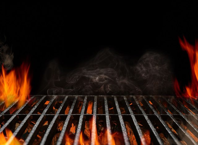 Hot empty portable barbecue BBQ grill with flaming fire and ember charcoal on black background. Waiting for the placement of your food. Close up