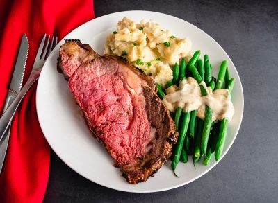 Prime Rib Served with Garlic Mashed Potatoes and Green Beans: Medium-rare prime rib dinner served with side dishes on a white plate