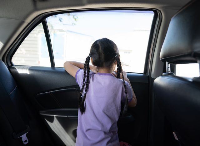 Backside of Little Asian 5 years old girl, is looking to the outside through car window mirror in the afternoon time.