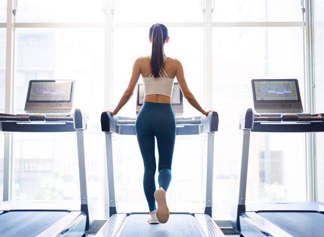 Rear view of young woman walking on treadmill