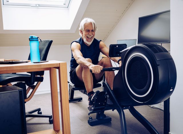 Indoor portrait of senior man working out on his rowing machine in his home office.