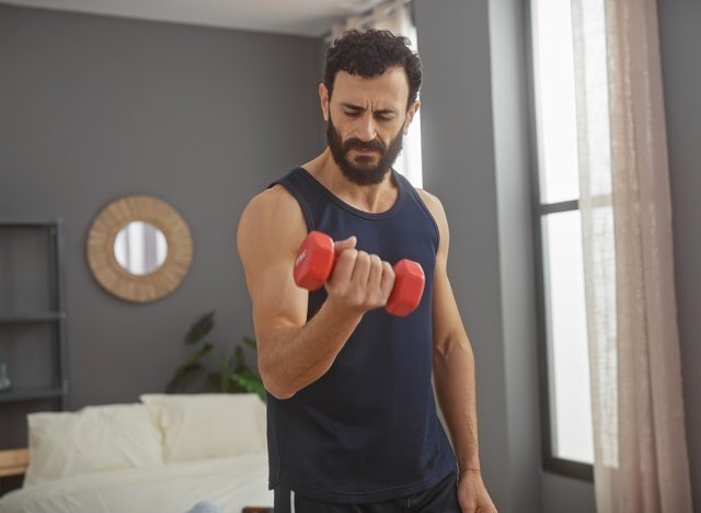 Middle-aged man exercising with dumbbell in a modern bedroom setting