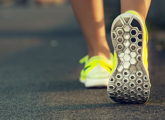 Runner woman feet running on road closeup on shoe. Female fitness model sunrise jog workout. Sports healthy lifestyle concept.