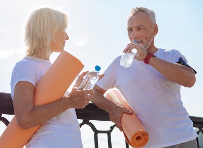 lderly couple discussing their yoga practice, drinking from water bottles