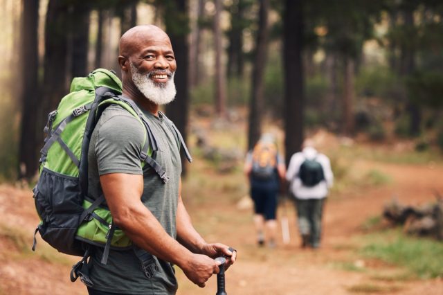 Portrait, black man and hiking in forest, exercise and fitness for wellness, healthy lifestyle and smile. Face, senior male and mature gentleman with backpack, smile and hiker in woods and fresh air