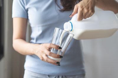 Young woman pouring milk to the glass in in the kitchen in the morning.