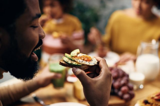 Man eating sandwich with avocado and eggs.